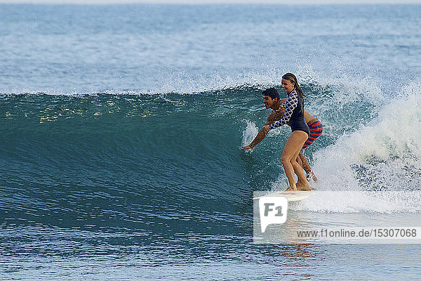 Junges Paar teilt sich ein Surfbrett und surft auf einer Meereswelle