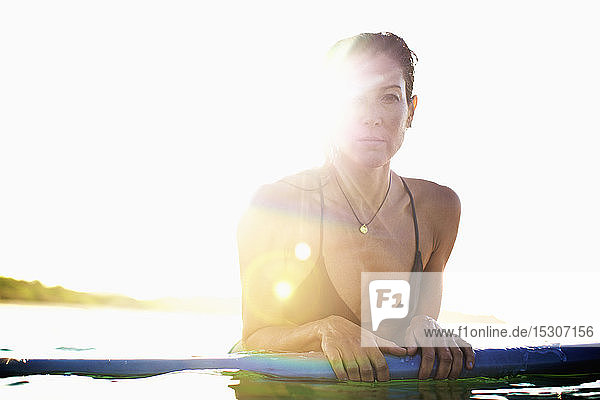 Porträt einer selbstbewussten Surferin  die sich auf ein Surfbrett im sonnigen Ozean stützt
