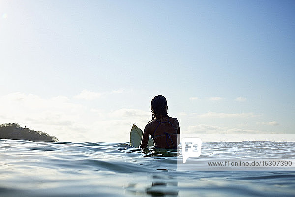 Silhouette einer weiblichen Surferin auf einem Surfbrett  die im sonnigen blauen Ozean wartet