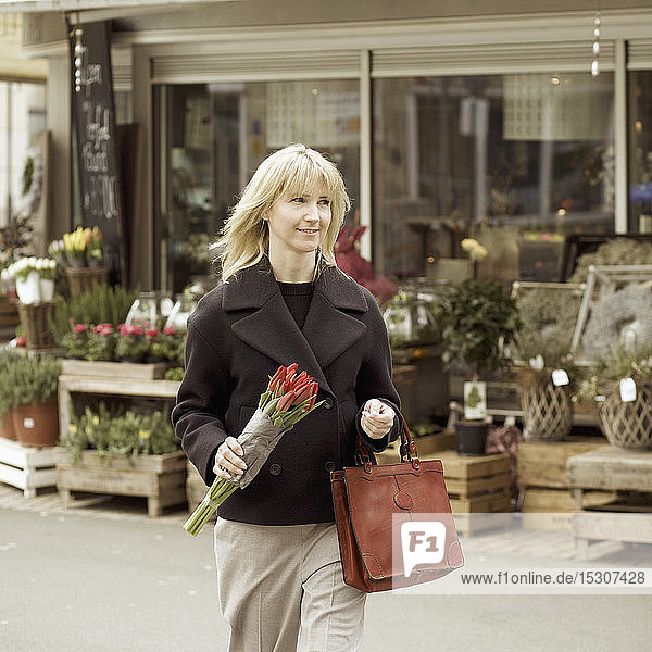 Woman carrying bunch of tulips on urban sidewalk