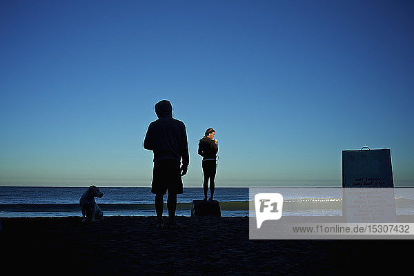 Silhouette junges Paar mit Hund am Strand bei Sonnenaufgang