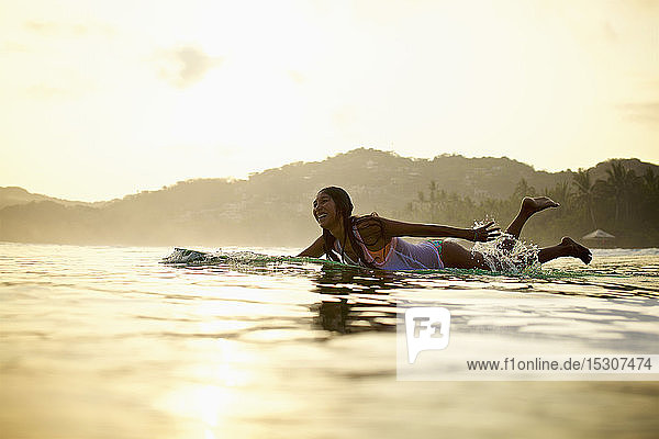 Happy female surfer paddling out in ocean on surfboard  Sayulita  Nayarit  Mexico