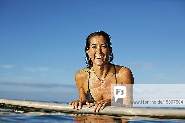 Porträt einer glücklichen  selbstbewussten Surferin  die sich auf ein Surfbrett im Meer stützt