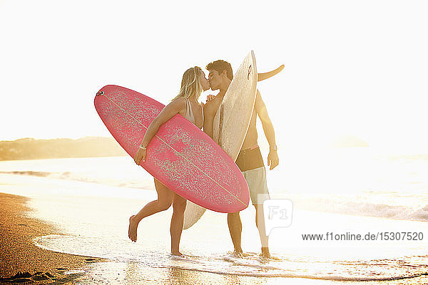 Junges  zärtliches Paar mit Surfbrettern küsst sich am sonnigen Meeresstrand