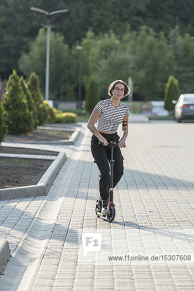 Young woman riding push scooter on sunny road