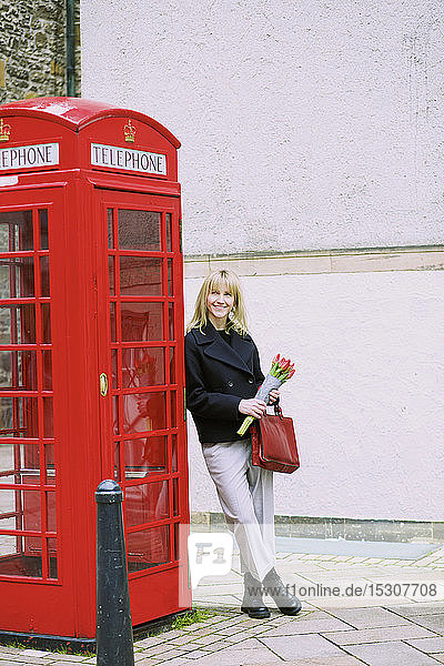 Woman with bunch of tulips leaning against red telephone box
