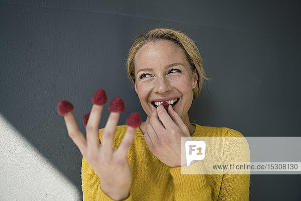 Blond woman with raspberries on her fingers  laughing