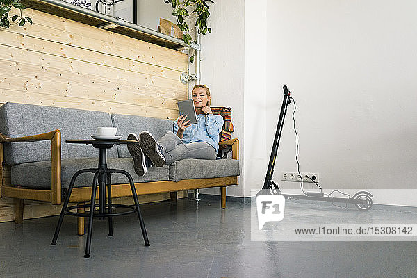 Young woman sitting on couch in a coffe shop  using digital tablet  e-scooter charging in background