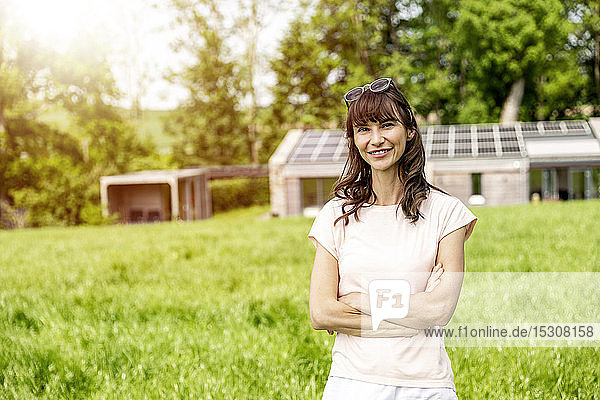 Porträt einer lächelnden Frau  die auf einer Wiese vor einem Haus steht