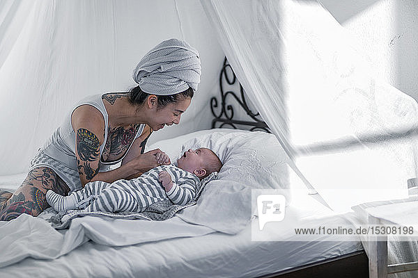 Tätowierte junge Frau mit ihrem Baby im Himmelbett