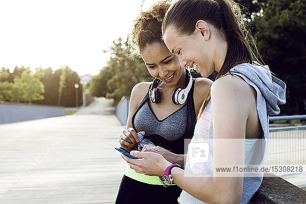 Two happy sporty young women checking cell phone