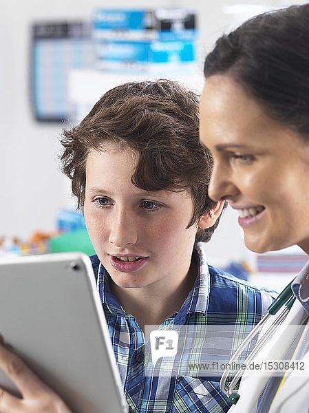 Ärztin zeigt einem jungen männlichen Patienten seine Laborergebnisse auf einem digitalen Tablett in der Klinik