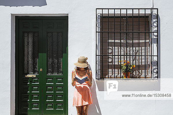 Redheaded young woman reading a book in front of a house Frigiliana Malaga Spain