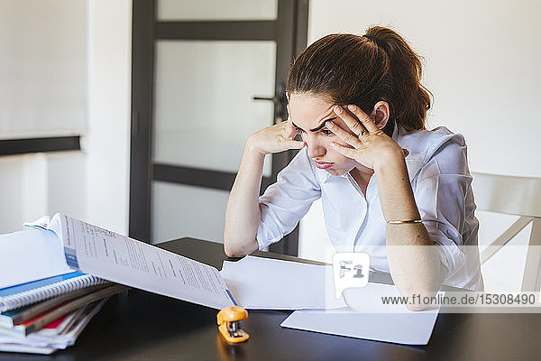 Frustrierte Studentin mit Dokumenten am heimischen Schreibtisch