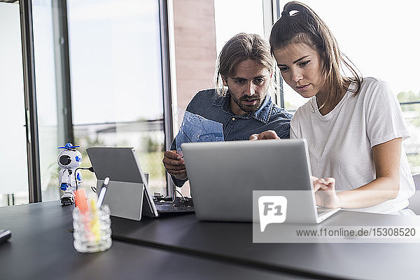 Young man and woman working together on laptop at desk in office