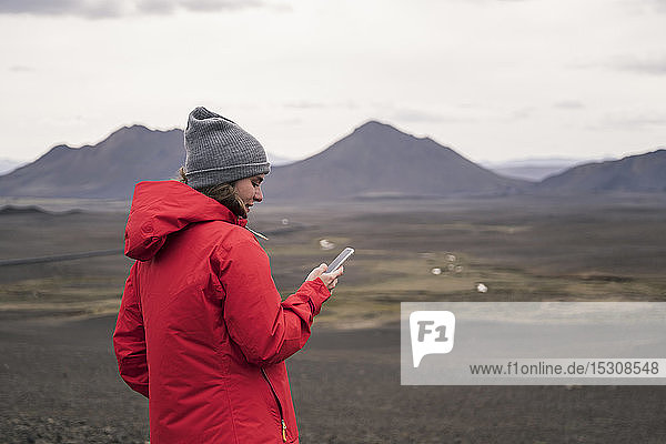 Junge Frau mit Smartphone im isländischen Hochland