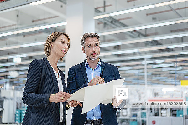 Businessman and businesswoman discussing plan in a factory hall