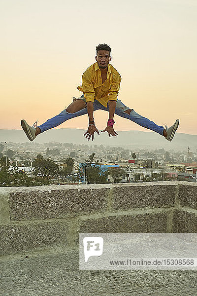 Young man in a yellow shirt jumping from a wall at sunset