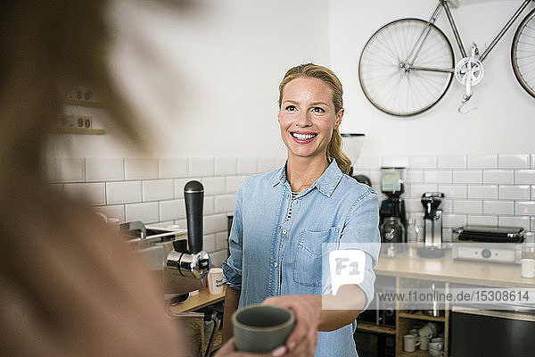 Jungunternehmerin in ihrem Kaffeehaus  die einem Kunden Kaffee serviert
