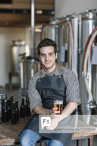 Porträt eines lächelnden jungen Mannes  der in einer Brauerei ein Bier trinkt