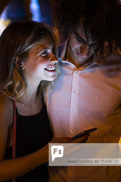 Glückliches junges Paar mit leuchtendem Handy in der Nacht