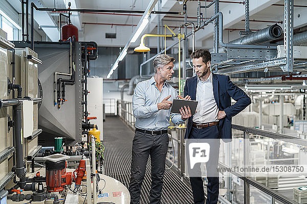 Zwei Geschäftsleute mit Tablette im Gespräch in einer modernen Fabrik