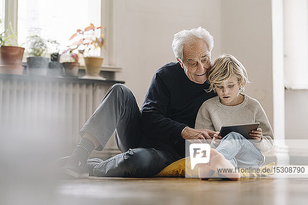 Grossvater und Enkel sitzen zu Hause auf dem Boden und benutzen ein Tablett