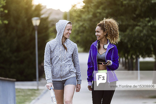 Zwei lächelnde sportliche junge Frauen gehen nach dem Training im Park spazieren