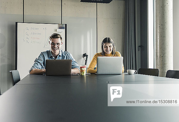 Happy businessman and businesswoman with laptops in conference room