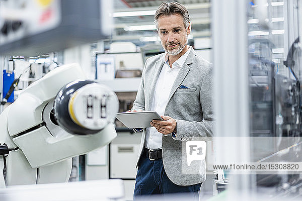 Businessman with tablet at assembly robot in a factory