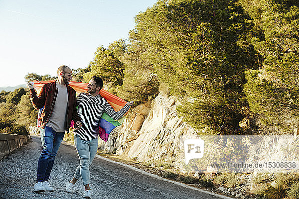 Homosexuelles Paar mit der Fahne Gay Pride geht auf einer Straße in den Bergen