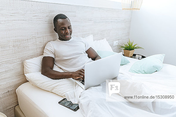 Junger Mann liegt zu Hause mit Laptop im Bett