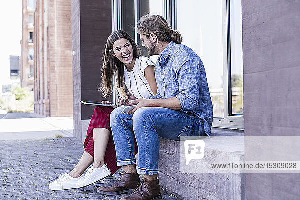 Young couple sitting on windowsill at a building using a tablet