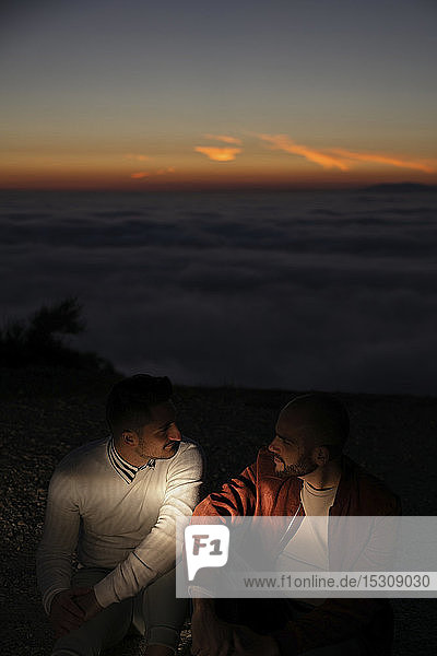 Schwules Paar sitzt bei Sonnenuntergang in den Bergen über den Wolken