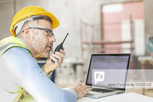 Architect using laptop and walkie talkie at construction site