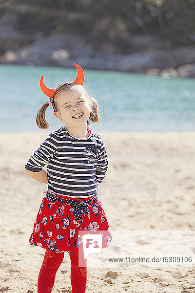 Portrait of girl standing on the beach wearing devil's horns