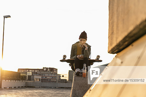 Stilvolle junge Frau mit Skateboard und Handy auf dem Parkdeck