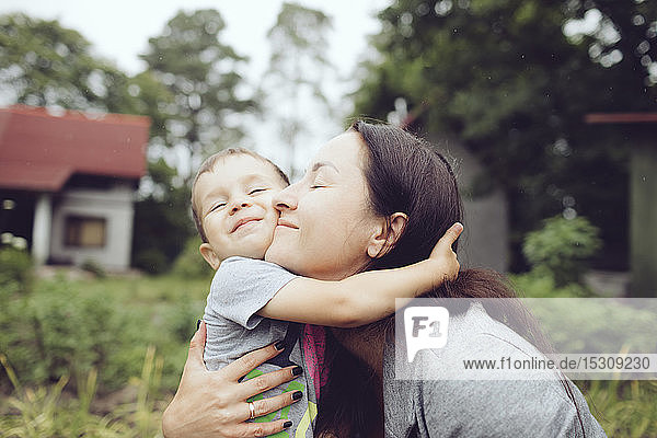 Affectionate mother hugging toddler in garden