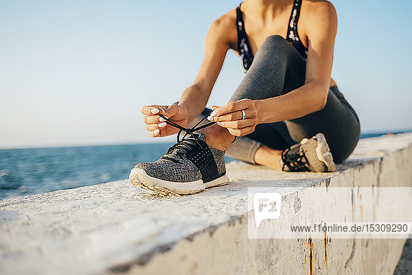 Sportswoman sitting on a wall and tying running shoe