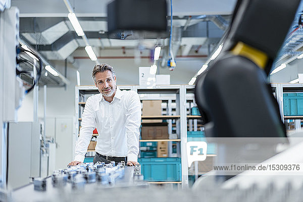 Selbstbewusster Geschäftsmann in einer modernen Fabrikhalle mit Blick auf Roboter