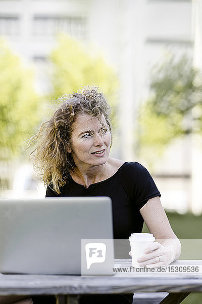 Porträt einer reifen Geschäftsfrau mit Laptop und Kaffee zum Draussengehen