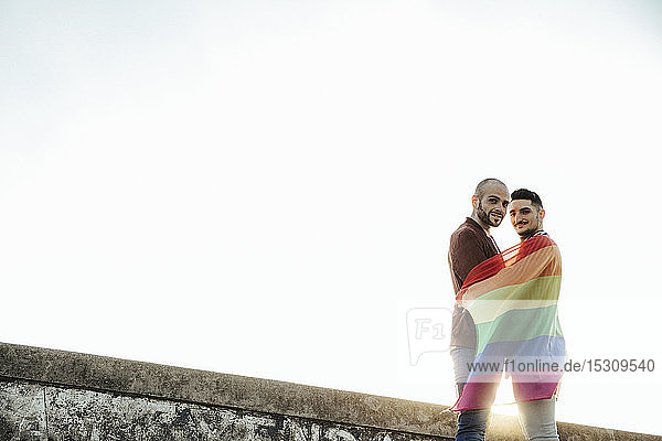 Porträt eines lächelnden schwulen Paares mit der Fahne des schwulen Stolzes