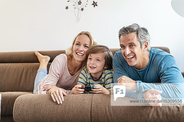 Glückliche Eltern mit Sohn spielen zu Hause auf der Couch Videospiele