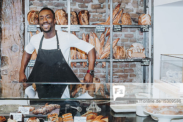 Lächelnder Mann  der in einer Bäckerei arbeitet und seine Schürze auszieht