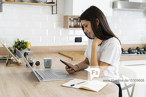 Young woman using cell phone and laptop at home
