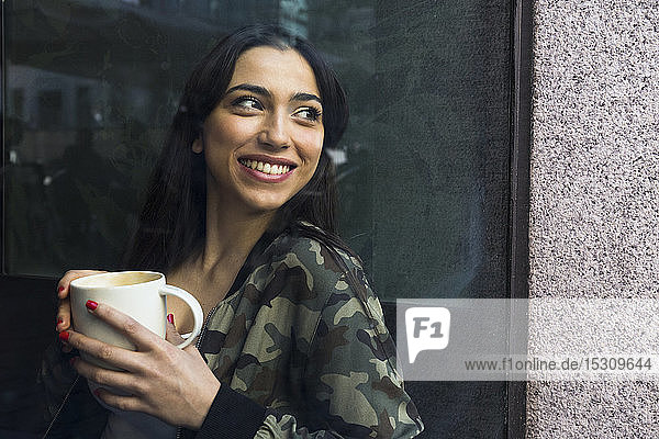 Young woman sitting in cafe with cup of coffee and looking out of window