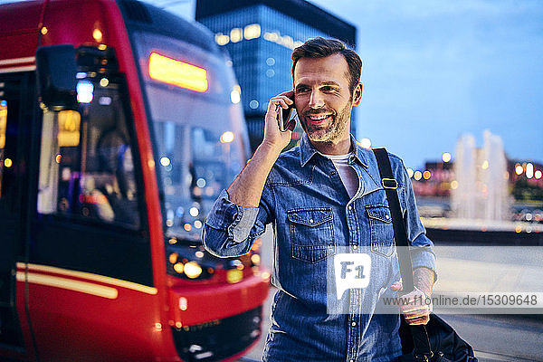 Mann telefoniert auf Smartphone mit der Straßenbahn im Hintergrund