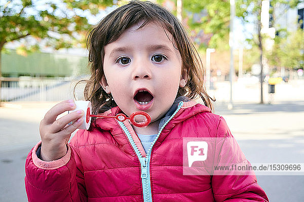 Porträt eines kleinen Mädchens  das im Freien Seifenblasen macht