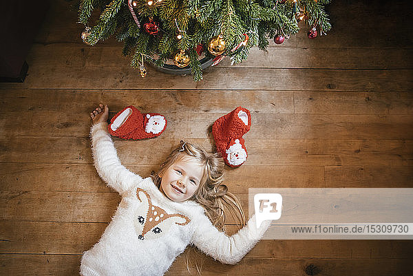 Lächelndes Mädchen unter dem Weihnachtsbaum liegend