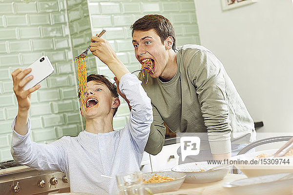 Brothers taking selfie in kitchen  eating spaghetti with tomato sauce
